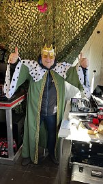 "Mann in grüner Königskutte mit Hermelinbesatz und goldener Krone steht lachend vor einem Mischpult und hebt beide Daumen hoch. (Foto: Autohaus Peter GmbH)