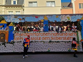 Seitenansicht des bunt gestalteten Karnevalswagens mit dem Schriftzug In jedem Märchen nah und fern fährt er stolz den Silberstern, mehrere verkleidete Menschen stehen darauf, zwei Personen in Narrenkostümen davor. (Foto: Autohaus Peter GmbH)