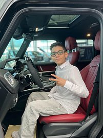 Jamil aus The Voice Kids sitzt auf dem Fahrersitz eines schwarzen Mercedes mit roter Lederausstattung, lächelt in die Kamera und zeigt ein Peace-Zeichen. (Foto: Autohaus Peter)
