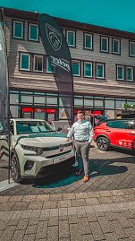 Ein Mann steht neben einem weißen Citroën-Ausstellungswagen vor einem Peugeot-Banner, im Hintergrund ein roter Opel. (Foto: Autohaus Peter)