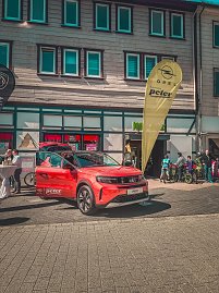 Roter Opel-Ausstellungswagen mit geöffneten Türen neben einem gelben Opel-Banner, Passanten und Kinder im Hintergrund. (Foto: Autohaus Peter)