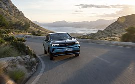 Türkis-schwarzer Opel Mokka Electric fährt auf einer kurvigen Küstenstraße bergauf, Blick frontal von vorn, Meer und Berge im Hintergrund. (Foto: Opel Automobile GmbH)