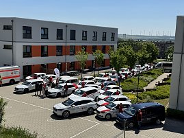 Gesamtansicht des DRK-Fuhrparks: Luftaufnahme des Innenhofs vor einem DRK-Gebäude mit zahlreichen Einsatzfahrzeugen, einem Rettungswagen und Mitarbeitenden, die neben den Autos stehen. (Foto: Autohaus Peter)