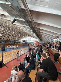 Innenaufnahme einer Sporthalle mit gefüllter Tribüne. Auf der Spielfläche stehen in Formation mehrere Sportlerinnen in weißen Anzügen bei einer Vorführung. (Foto: Autohaus Peter)