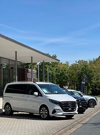 Ein weißer Mercedes-Benz Van ist vor der Stadthalle Wittenberg geparkt, dahinter ein weiteres schwarzes Fahrzeug und eine Mercedes-Fahne. (Foto: Autohaus Peter)