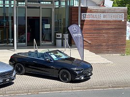 Ein schwarzes Mercedes-Benz Cabriolet steht vor der Stadthalle Wittenberg neben einer Mercedes-Fahne. Das Dach ist geöffnet, der Innenraum ist zu sehen. (Foto: Autohaus Peter)