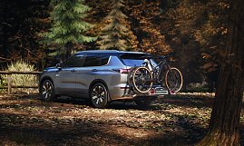 Mit Fahrradträger: Heckansicht des Mitsubishi Outlander mit montiertem Fahrradträger und zwei Fahrrädern, geparkt in einem Waldgebiet. (Foto: Mitsubishi Motors)