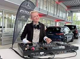 DJane mit Kopfhörern steht an einem Pioneer-DJ-Pult in einer Mercedes-Benz Ausstellungshalle und lächelt in die Kamera. (Foto: Eric Freytag)