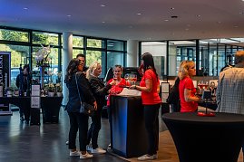 Mehrere Frauen, teils in roten „Shes Mercedes“-T-Shirts, teils in schwarzen Outfits, stehen an einem Stehtisch mit Gläsern und unterhalten sich in einem hellen Autohaus. (Foto: Eric Freytag)
