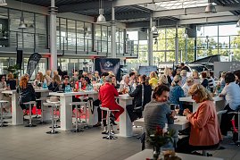 Publikum im Showroom: Viele Frauen sitzen an hohen weißen Tischen in einem großen, hellen Autohaus mit Glasfront, trinken und unterhalten sich. Im Hintergrund sind Mercedes-Werbematerialien und Fahrzeuge sichtbar. (Foto: Eric Freytag)