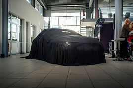  Ein Mercedes-Fahrzeug ist vollständig mit einem schwarzen Tuch bedeckt, auf dem „Autohaus Peter“ steht, in einem hellen Ausstellungsraum. (Foto: Eric Freytag)