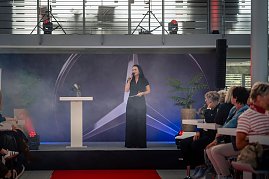 Christina Dost spricht auf einer Bühne mit Mercedes-Logo im Hintergrund, rotem Teppich davor und Publikum auf beiden Seiten. (Foto: Eric Freytag)