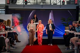 Drei Frauen laufen in modischen Outfits über einen roten Teppich auf einer Bühne mit Mercedes-Logo, während eine Moderatorin am Pult steht. Das Publikum applaudiert. (Foto: Eric Freytag)