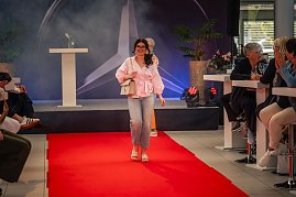 Eine junge Frau mit langen, dunklen Haaren, rosa Bluse, hellen Jeans und beiger Handtasche läuft lächelnd über den roten Teppich. (Foto: Eric Freytag)