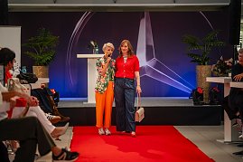  Moderatorin in farbenfrohem Blazer mit einer Frau im roten Oberteil, gestreiftem Shirt und weiter Jeans am Ende des Laufstegs. (Foto: Eric Freytag)