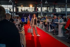 Frau im beigefarbenen Hosenanzug mit braunem Oberteil und großem, silberfarbenem Shopper läuft auf dem roten Teppich. (Foto: Eric Freytag)