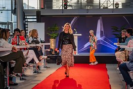  Frau mit blonden Haaren, schwarzem Oberteil, schwarzer Jacke und Leopardenrock trägt eine schwarze Handtasche über den Laufsteg. (Foto: Eric Freytag)