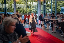 Frau mit kurzem blondem Haar, weißer Jacke und langem, dunkelblauem Kleid mit weißen Punkten läuft über den roten Teppich. (Foto: Eric Freytag)