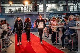 Mehrere Models in sportlicher Kleidung  schwarze Jacken mit roten und weißen Akzenten  laufen gleichzeitig über den roten Teppich, ein junger Mann und eine junge Frau vorne, weitere Personen dahinter. (Foto: Eric Freytag)