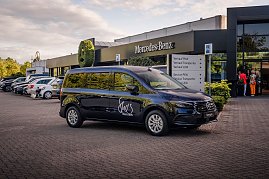Schwarzer Mercedes-Van mit „Shes Mercedes“-Logo vor einem Mercedes-Benz Autohaus geparkt. Im Hintergrund stehen weitere Fahrzeuge und einige Menschen am Eingang. (Foto: Eric Freytag)
