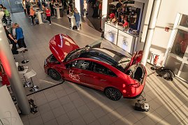 Von oben fotografierter roter Mercedes mit „Shes Mercedes“-Logo, Motorhaube und Kofferraum geöffnet. Im Autohaus sind Besucher an Stehtischen und einem Catering-Stand zu sehen. Mercedes-Benz CLA 250+ mit EQ-Technologie | Energieverbrauch kombiniert: 14,1-12,2 kWh/100 km | CO2Emissionen kombiniert: 0 g/km | CO2-Emissionsklasse: A (Foto: Eric Freytag)
