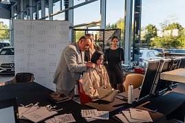 Friseurmeister in grauem Anzug hält die Haare einer sitzenden Frau und schlägt ihr eine Frisur vor, während zwei weitere Frauen zusehen. Vor ihnen stehen Kosmetik- und Styling-Utensilien auf Tischen. (Foto: Eric Freytag)