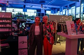 Zwei Frauen stehen im Autohaus vor einem Kleiderständer und lächeln in die Kamera, links eine in grauem Hosenanzug, rechts Mandy Kossira in bunter Jacke mit Blumenmuster. (Foto: Eric Freytag)