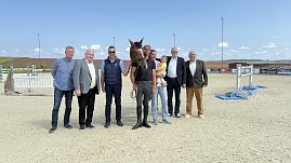 Pressekonferenz auf dem Reitplatz in Immenrode: Sieben erwachsene Personen stehen nebeneinander, darunter ein Reiter mit Pferd und eine Person mit Kind auf dem Arm. Im Hintergrund sind Hindernisse und die Reitplatzanlage zu sehen. Die Veranstaltung dient der offiziellen Vorstellung des Reitturniers Immenrode 2025. (Foto: Depping/Autohaus Peter)