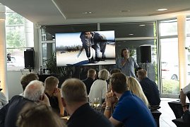Abenteuer-Guide Hannu präsentiert beim südafrikanischen Abend im Autohaus Peter in Heiligenstadt spannende Eindrücke einer Safari, während auf dem Bildschirm ein Elefant zu sehen ist und die Gäste aufmerksam zuhören. (Foto: Peter Gruppe)