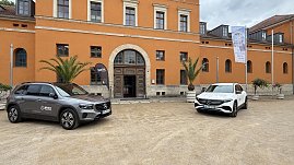 Zwei Mercedes-Benz SUVs, ein graues und ein weißes Modell, parken vor einem historischen Gebäude mit orangefarbener Fassade. Vor dem Eingang stehen Palmen in großen Pflanzkübeln und ein Werbefähnchen von Autohaus Peter. (Foto: Autohaus Peter)