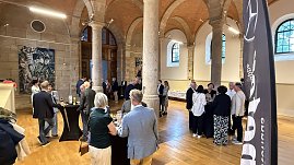 Innenaufnahme eines historischen Saals mit hohen Steinsäulen und Holzboden. Gäste stehen an Stehtischen, unterhalten sich und genießen Getränke. Im Hintergrund ist ein Buffet aufgebaut. (Foto: Autohaus Peter)