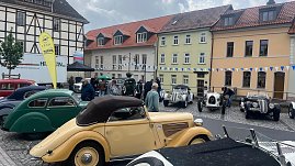 Mehrere Oldtimer stehen auf dem Marktplatz von Sondershausen vor einer Häuserzeile mit bunten Fassaden. Zu sehen sind historische Fahrzeuge in verschiedenen Farben und Karosserieformen  unter anderem ein cremefarbenes Cabriolet im Vordergrund. Menschen schlendern zwischen den Autos. (Foto: Autohaus Peter)