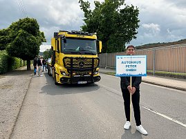 Ein junger Mann steht auf einer Straße und hält ein Schild mit der Aufschrift „Autohaus Peter GmbH“ bei einem Festumzug in Sondershausen anlässlich „900 Jahre Sondershausen“. Hinter ihm steht ein gelber Mercedes-Benz Abschlepp-Lkw mit der Aufschrift „Peter“ auf der Windschutzscheibe. Weitere Personen und Fahrzeuge sind im Hintergrund zu sehen. (Foto: Autohaus Peter)