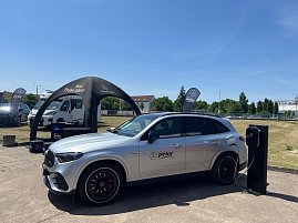 Ein silberner Mercedes-Benz SUV mit Autohaus-Peter-Logo steht bei einer Präsentation im Freien am Ladegerät. Im Hintergrund sind ein schwarzes Zelt mit der Aufschrift Jetzt Probe fahren, Fahnen und weitere Fahrzeuge zu sehen. Die Szene gehört zum Leichtathletik-Meeting Anhalt 2025. (Foto: Autohaus Peter )