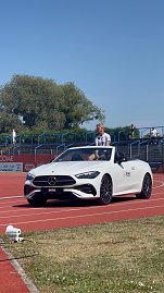 Ein weißes Mercedes-Benz Cabrio des Autohauses Peter fährt über die rote Laufbahn beim Leichtathletik-Meeting Anhalt 2025. Ein Sportler sitzt darin; im Hintergrund sind Zuschauertribünen und Bäume zu sehen. (Foto: Autohaus Peter )