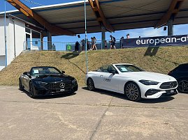  Zwei Mercedes-Benz Cabriolets, eines schwarz und eines weiß, stehen nebeneinander auf einem befestigten Platz beim Leichtathletik-Meeting Anhalt 2025. Hinter den Fahrzeugen verläuft ein Grashang mit Zuschauern und einer überdachten Tribüne. (Foto: Autohaus Peter )