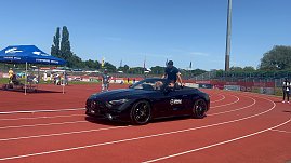 Ein schwarzes Mercedes-AMG Cabrio des Autohauses Peter fährt mit einem Sportler über die Laufbahn im Stadion des Anhalt 2025 Leichtathletik-Meetings. Im Hintergrund sind das blaue Zelt der Stadtwerke Dessau, einige Zuschauer und die Beschilderung mit WELCOME und BIENVENUE zu sehen. (Foto: Autohaus Peter )