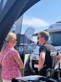 Ein Mitarbeiter des Autohauses Peter spricht auf dem Anhalt 2025 Leichtathletik-Meeting mit einer Besucherin. Im Hintergrund stehen mehrere Mercedes-Benz Fahrzeuge sowie Fahnen und ein Wohnmobil. Die Szene findet unter freiem Himmel bei sonnigem Wetter statt. (Foto: Autohaus Peter )