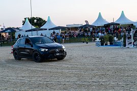 Ein schwarzer Mercedes-Benz SUV fährt über den Sandplatz einer Reitanlage. Im Hintergrund sitzen zahlreiche Zuschauer unter weißen Pagodenzelten und schwarzen Sonnenschirmen und verfolgen das Abendprogramm des Turniers. [Mercedes-AMG GLA 35 4MATIC | Energieverbrauch kombiniert: 9,3-8,8 l/100 km | CO2-Emissionen kombiniert: 211-200 g/km | CO2-Klasse: G] (Foto: Autohaus Peter)