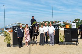 Siegerehrung beim Reitturnier in Immenrode: Ein Reiter sitzt auf seinem Pferd mit Siegerdecke und Blumenstrauß, daneben stehen fünf Erwachsene zur Gratulation. Die Szene spielt sich zwischen Mercedes-Benz-Hindernissen und unter wehenden Fahnen auf dem Turnierplatz ab. (Foto: Autohaus Peter)