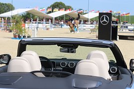 „Blick über die Sitze eines schwarzen Mercedes-Benz Cabrios auf den Springplatz beim Reitturnier in Immenrode. Im Hintergrund springt ein Reiter über ein Hindernis, flankiert von Mercedes-Benz-Werbebannern und zahlreichen Länderflaggen. (Foto: Autohaus Peter)