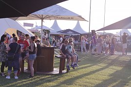 Besucher genießen den Abend auf der Wiese beim Reitturnier in Immenrode. Unter großen Sonnenschirmen und Pagodenzelten stehen Gruppen zusammen, einige Gäste sitzen an Stehtischen oder auf Bänken. (Foto: Autohaus Peter)