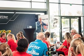 Bodo Ramelow spricht beim Medien-Tag des Thüringer HC in Erfurt. Er steht mit Mikrofon in der Hand an einem Stehtisch vor einem Publikum aus Spielerinnen und Gästen, die überwiegend rote Shirts tragen. Im Hintergrund Banner mit dem Logo des Thüringer HC. (Foto: Autohaus Peter)