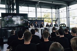 Podium mit sieben Mitgliedern der Geschäftsführung und Ausbildungsleitung der Autohaus-Peter-Gruppe bei der Begrüßung der neuen Auszubildenden. Davor sitzen Azubis in schwarzen T-Shirts und hören zu. (Foto: Autohaus Peter)