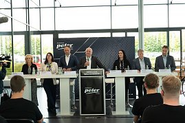 Podium mit sieben Mitgliedern der Geschäftsführung und Ausbildungsleitung der Autohaus-Peter-Gruppe bei der Begrüßung der neuen Auszubildenden. Davor sitzen Azubis in schwarzen T-Shirts und hören zu. (Foto: Autohaus Peter)
