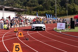 Weißes Mercedes-Cabrio fährt auf die rote Tartanbahn des Stadions ein. Auf dem Rücksitz sitzen mehrere Sportlerinnen, während Zuschauer am Rand applaudieren. (Foto: Autohaus Peter)