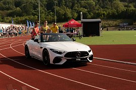 Nahaufnahme des weißen Mercedes-Cabrios auf der Laufbahn. Drei Sportstars sitzen auf der Rückbank, jubeln und winken dem Publikum zu. (Foto: Autohaus Peter)