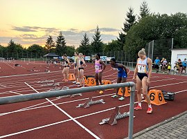 Sechs Sprinterinnen stehen an ihren Startblöcken auf der Laufbahn. Der Himmel im Hintergrund zeigt einen Sonnenuntergang mit Wolken. (Foto: Autohaus Peter)
