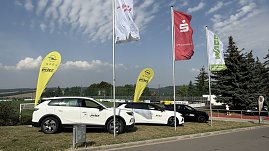 Zwei weiße und ein schwarzes Opel-Fahrzeug vom Autohaus Peter stehen nebeneinander auf dem Rasen auf dem Weg zum Stadion. Daneben gelbe Opel-Werbebanner sowie Fahnen der Kyffhäusersparkasse, WAGO und weiterer Sponsoren. (Foto: Autohaus Peter)