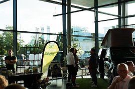 Ein Messestand mit gelb-grünem Banner „Möbius  Grün macht glücklich!“. Daneben ein schwarzer Mercedes-Camper mit hochgeklapptem Dach. Zwei Männer und weitere Personen unterhalten sich. (Foto: Buchardt | Autohaus Peter )